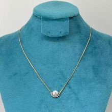Collier doré orné d'un pendentif en perle entourée de petites pierres lumineuses